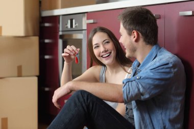 Mutfak zemininde oturan yeni ev anahtarlarını gösteren mutlu kiracılar.