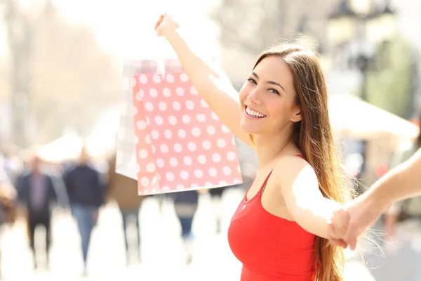 快乐的购物者牵着她的伴侣手牵着购物袋走在大城市的大街上 — 图库照片