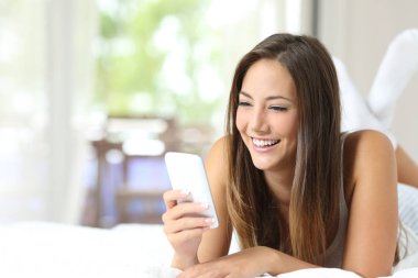 Mutlu kız evde akıllı bir telefonla yatakta yatıyor.