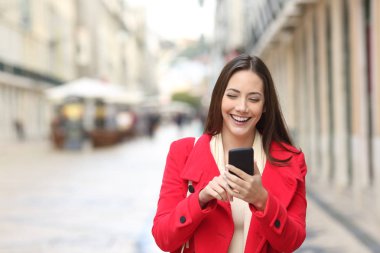 Akıllı telefon sokakta kışın kullanarak yürüyüş kırmızı mutlu bir kadın önden görünümü