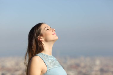 Arka planda bir şehirle derin temiz hava soluyan mutlu kadın.