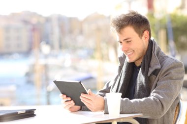 Sahil kasabasındaki bir kafede tablet kullanan mutlu bir adam. 