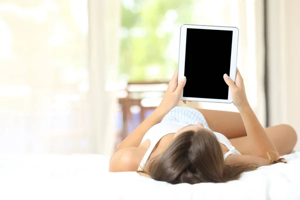 一个女孩躺在床上观看并显示一个空白平板电脑屏幕的全身肖像 — 图库照片