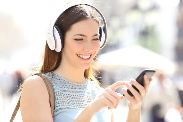 幸せな女の子は音楽を聞いてスマートフォンのコンテンツを閲覧通りを歩く — ストック写真