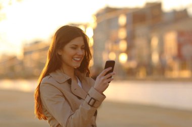Sokakta günbatımında bir akıllı telefon kullanan kadın