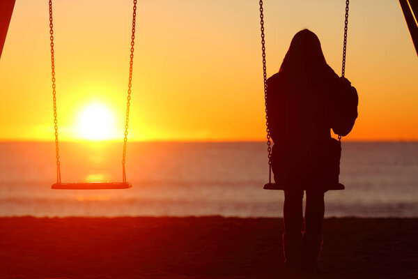 Back view portrait of a single woman silhouette sitting on a swing contemplating sunset