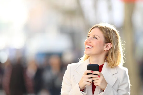 Szczęśliwa Kobieta Patrząc Bok Trzymając Smartfon Stojący Ulicy — Zdjęcie stockowe