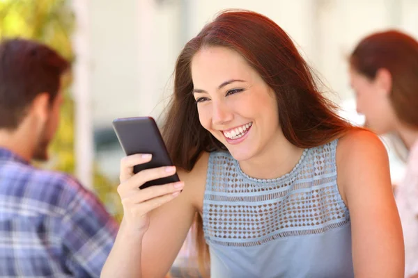 快乐的女人坐在酒吧的阳台上 用智能手机读着留言 — 图库照片