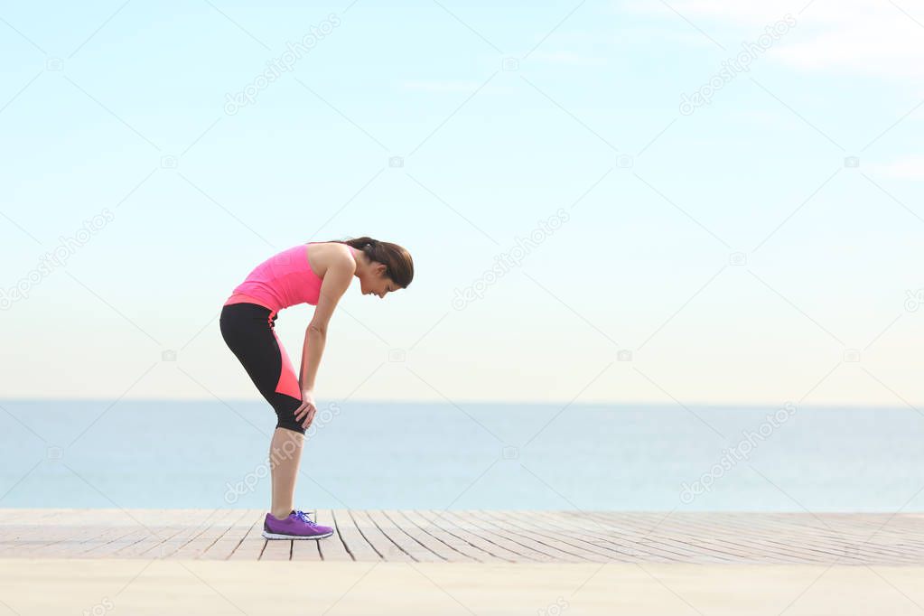 Side view portrait of an exhausted runner resting on the beach after exercise