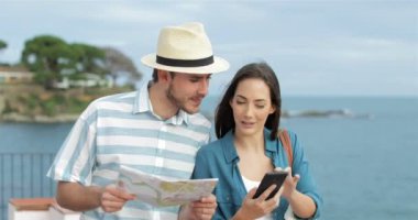 Mutlu çift karşılaştırma akıllı telefon içerik ve kağıt harita sahilde yürüyen turist