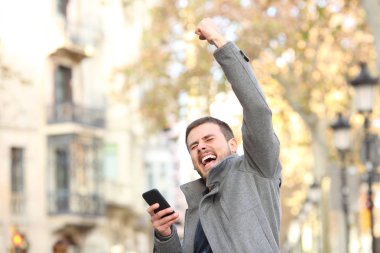 Akıllı telefon tutarak ve sokakta kol yükselterek heyecanlı bir adam portresi