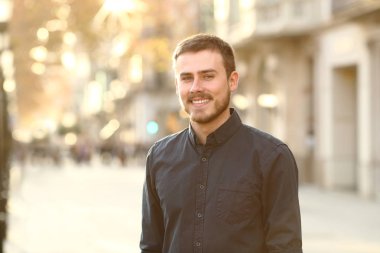 Mutlu adam sokakta poz veriyor. Gün doğumunda sıcak bir ışıkla kameraya bakıyor.