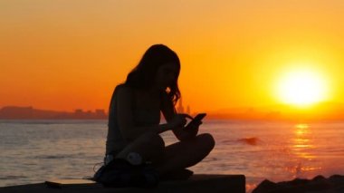 Heyecanlı bir öğrenci batımında sahilde bir akıllı telefon üzerinde iyi online haber okuma silüeti