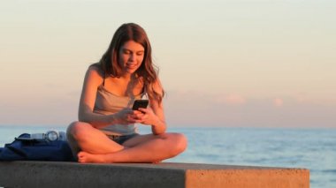 Mutlu genç öğrenci manifatura sahilde günbatımı, akıllı telefon