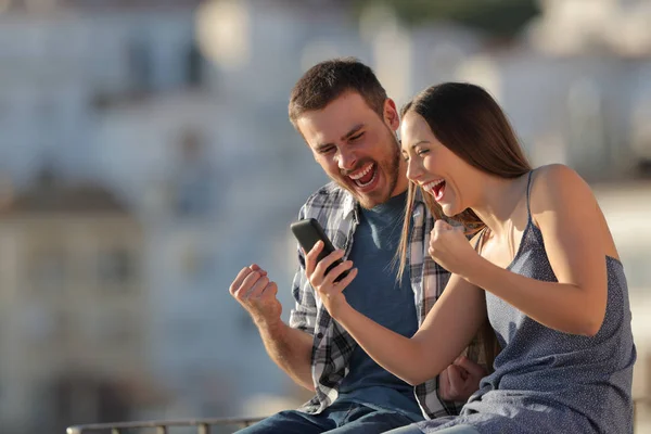 興奮したカップルや友人が夕暮れ時に町でスマートフォンのコンテンツを読む — ストック写真