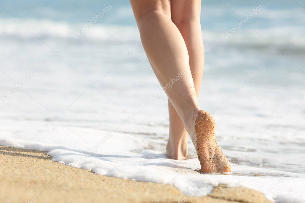 Back view portrait of a beautiful girl legs walks on the sand and sea water on the beach