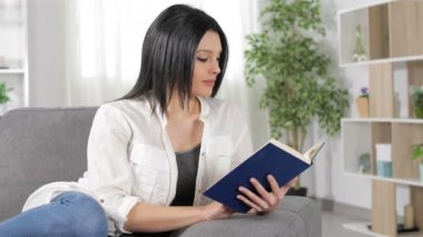 Ciddi kadın oturma odasında evde bir kanepede oturan bir kitap okuma