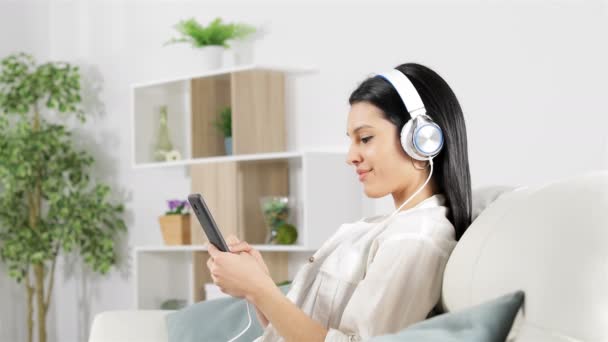 一个女人坐在家里的沙发上放松地听音乐的侧视图 — 图库视频影像