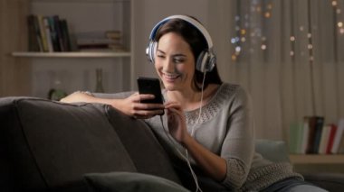 Mutlu kadın evde bir kanepede oturan gece akıllı telefon üzerinde müzik dinleme
