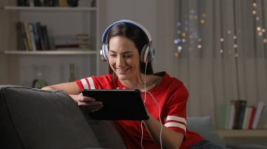 Gece evde bir kanepede oturan tablet medyada dinliyor ve izliyorlar mutlu teen