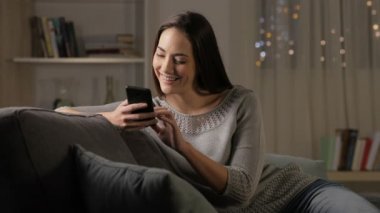 Gece evde bir kanepede oturan akıllı telefon kullanan mutlu kadın