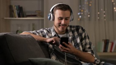 Mutlu adam akıllı telefon gece evde bir kanepede oturan müzik dinlemek