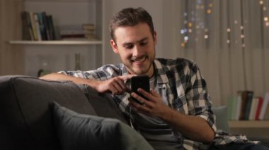 Mutlu adam akıllı telefon üzerinde bir kanepe n oturma odası gece evde oturan kullanarak