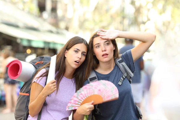 Two backpackers suffering heat stroke walking on the street and fanning on summer vacation