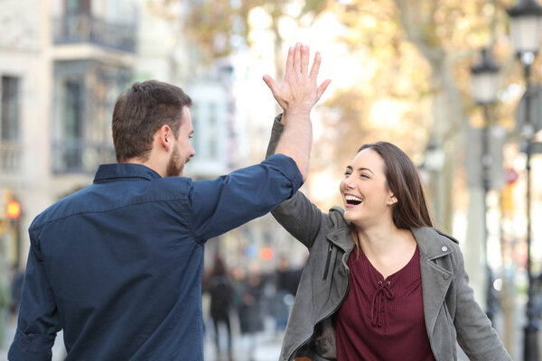 Two excited friends or couple giving high five in a city street