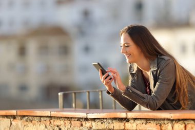 Mutlu kadın bir akıllı telefon bir balkonda günbatımında bir kasabada kullanır