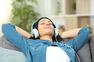 Rahatlamış kadın dinleniyor müzik dinliyor evdeki oturma odasında bir kanepede oturuyor.