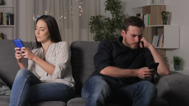 愤怒的夫妇使用他们的智能手机后 辩论坐在沙发上在家里的夜晚 — 图库视频影像