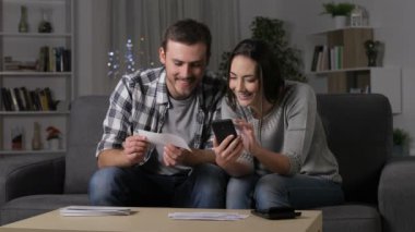 Mutlu çift bilgisi online akıllı telefon gece evde bir kanepede oturan karşılaştırma