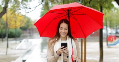 Telefon yağmur altında kontrol sokakta yürüyen bir mutlu kadın önden görünümü
