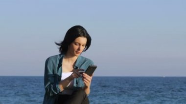 Heyecanlı kadın sahilde bir bankta oturmuş akıllı telefon üzerinde iyi haber bulma