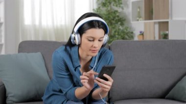 Mutlu kadın oturma odasında evde bir kanepede oturan cep telefonundan müzik