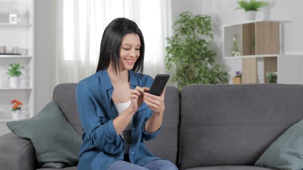 Glückliche Frau Mit Smartphone Auf Einem Sofa Heimischen Wohnzimmer Sitzend — Stockvideo