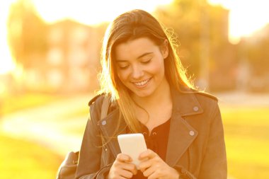Sokakta bir akıllı telefon kullanarak gün batımında mutlu bir genç kız portresi önden görünüm