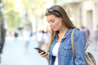 Şehir sokağında duran akıllı telefon içeriğini kontrol eden bekar bir kız.
