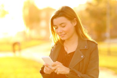 Genç kız sokakta akıllı telefonunu kullanarak gün batımında rahat