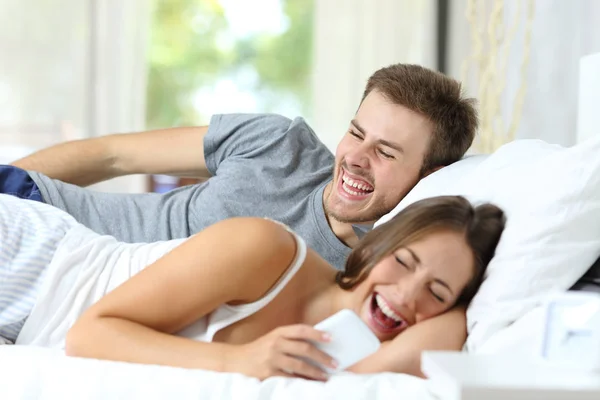 Ευτυχισμένο Ζευγάρι Ξαπλωμένη Στο Κρεβάτι Γέλιο Βλέποντας Περιεχόμενο Έξυπνο Τηλέφωνο — Φωτογραφία Αρχείου