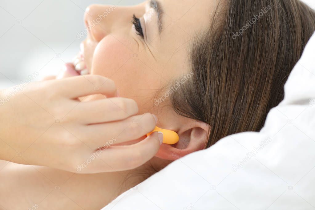 Close up of a woman hand putting ear plugs to sleep on a bed at home