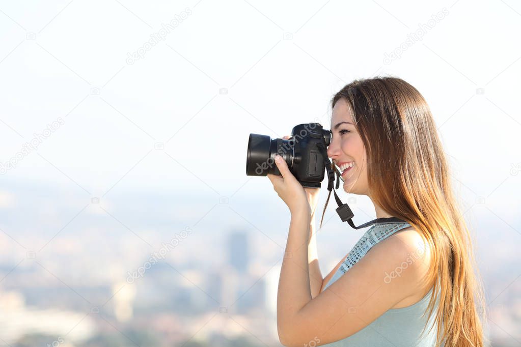 Side view portrait of a happy photographer taking photos with a dslr camera outdoors