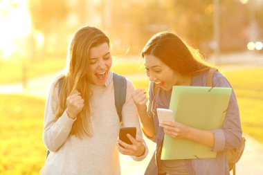 İki heyecanlı öğrenci günbatımında zeki telefon bir parkta iyi haber online bulma