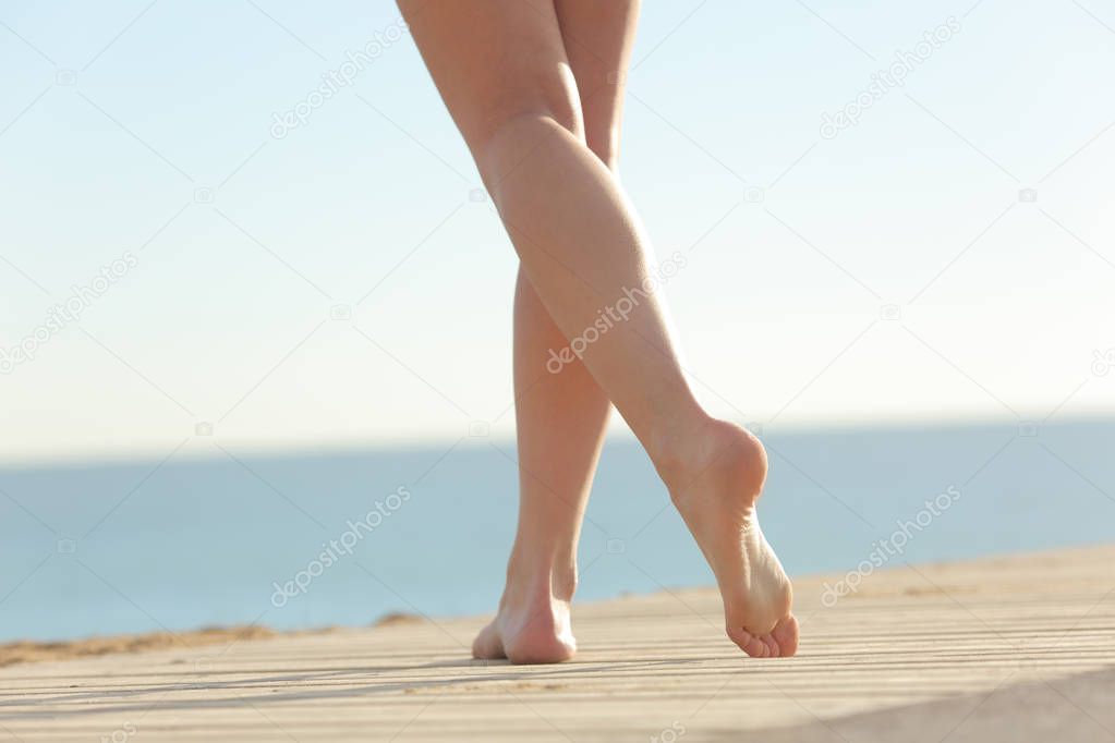 Close up of a woman waxed legs walking on the beach on a wooden floor