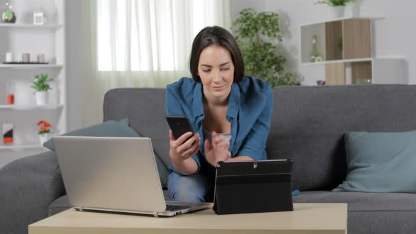 严肃的妇女使用多种设备坐在家里客厅的沙发上 — 图库视频影像