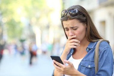 Üzgün kız sokakta duran akıllı telefon içeriğini kontrol ediyor.