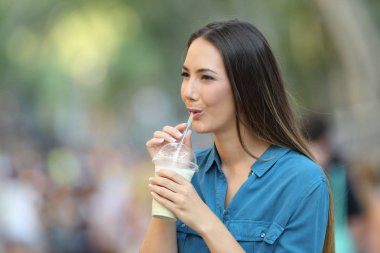 Milk shake yudumlayan mutlu kadın sokakta yürüyor.