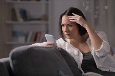 Endişeli kız, evdeki bir kanepede oturan akıllı telefon içeriğini kontrol ediyor.