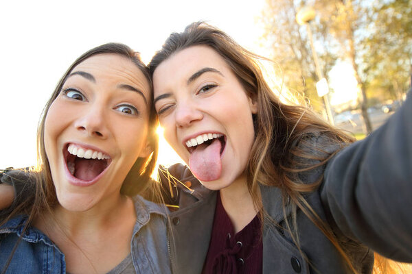 Two funny women joking taking selfies looking at camera in the street